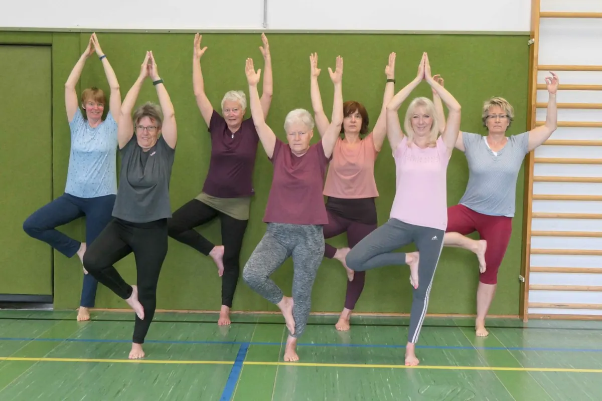 Eine Frauengruppe steht in der Halle im Baum, die Arme über dem Kopf